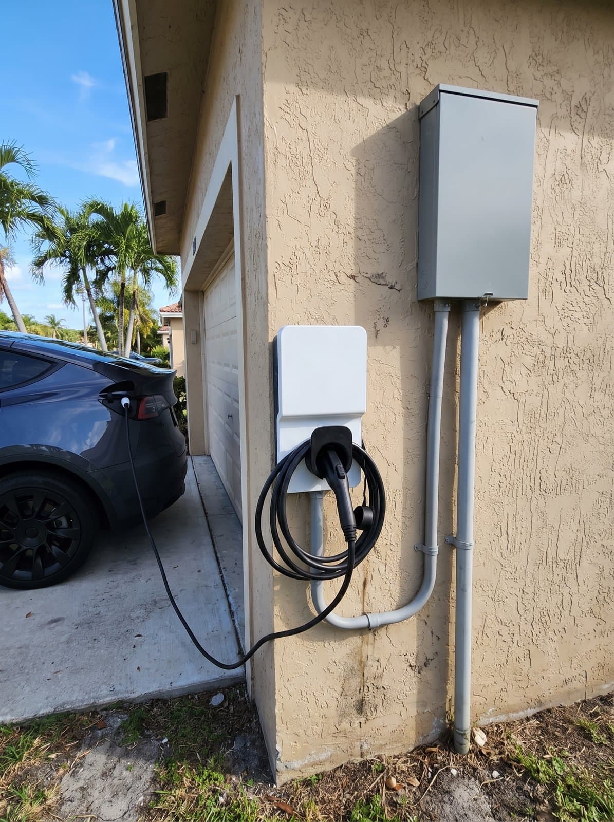 A Level 2 EV charger installed on the stucco wall of a South Florida home, cable plugged into a parked electric SUV