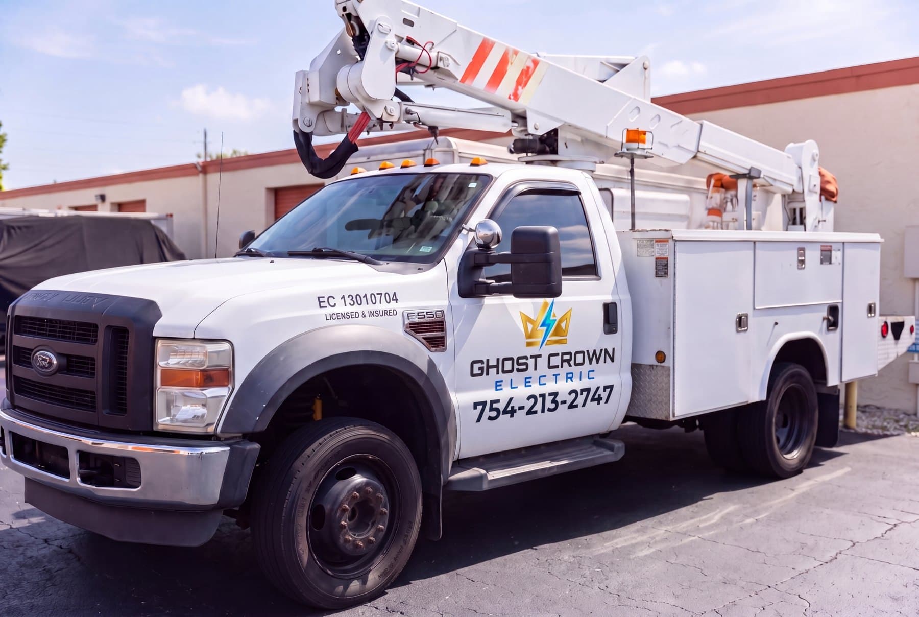 The Ghost Crown Electric bucket truck, decaled with the crown logo, company name, and phone number, parked at a commercial building
